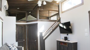 A spacious living area with a high ceiling, a staircase, a flat-screen TV mounted on the wall, and a large bed. - Outcast Landing - A Fisherman's Paradise (Cedar Creek)