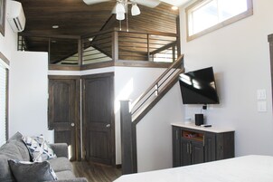 Amplia sala de estar con techo alto, escalera, televisor de pantalla plana montado en la pared y una cama grande.
