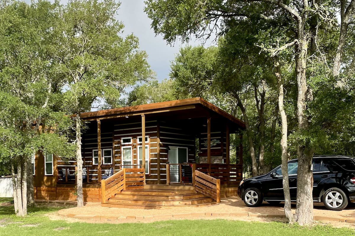 A log cabin with a wooden porch and a car parked nearby.