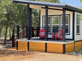 Un espacio de estar al aire libre cubierto con una terraza de madera y barandilla metálica, con dos sillas rojas y una mesa.