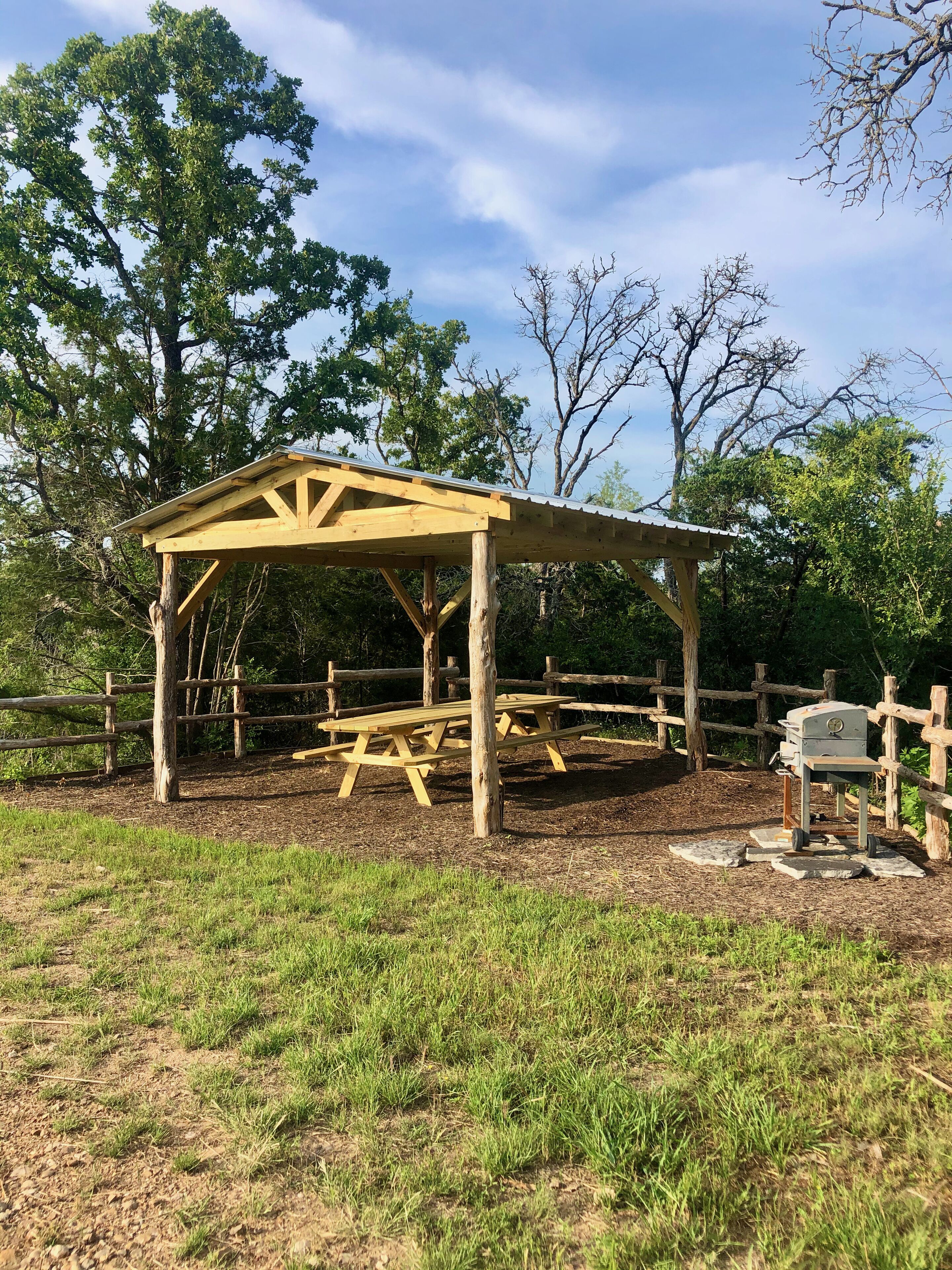 A wooden pavilion with a roof, surrounded by a wooden fence, and picnic tables inside.