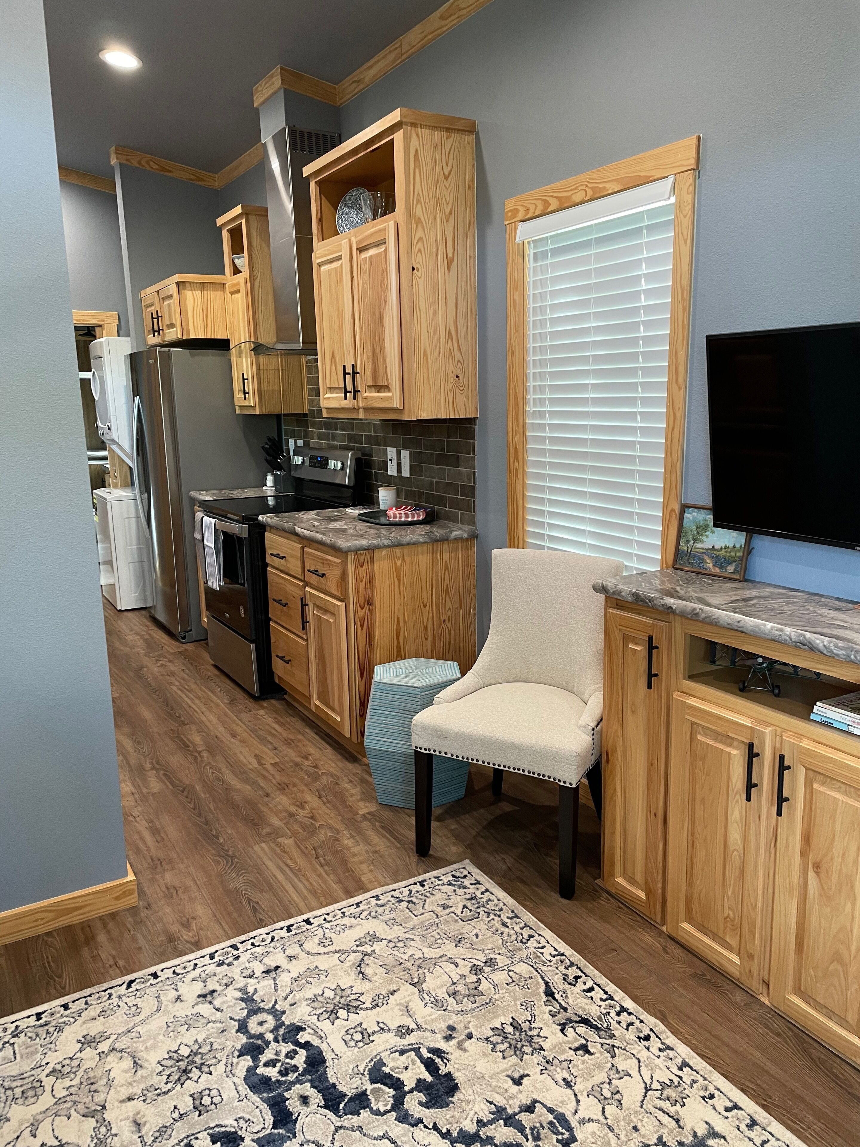 A modern kitchen with wooden cabinets, a built-in oven, and a large window with blinds.