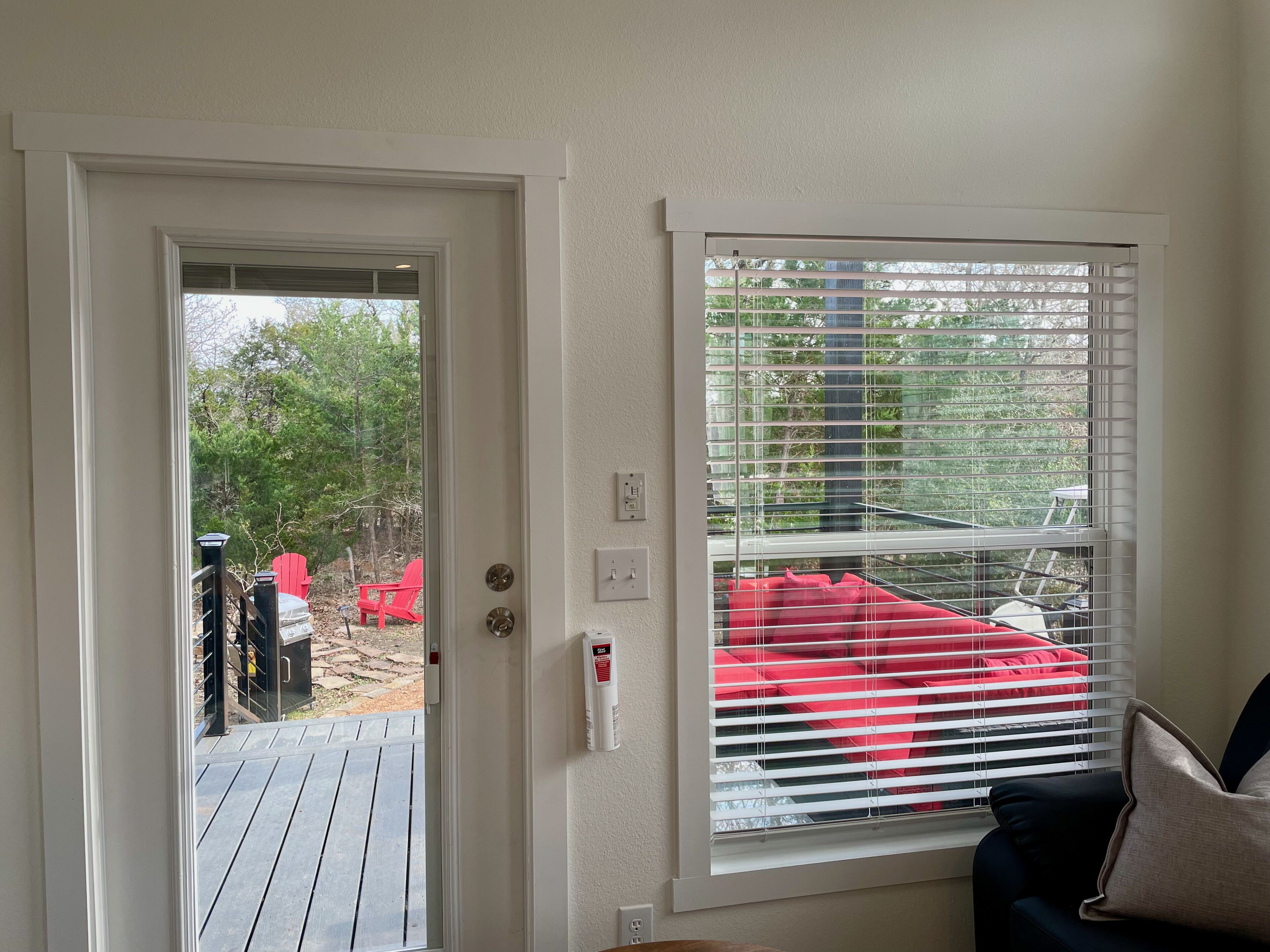 Una habitación con una puerta que da a una terraza al aire libre, una ventana con persianas y una silla roja afuera.