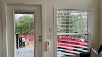 A room with a door leading to an outdoor deck, a window with blinds, and a red chair outside.
