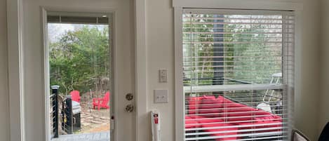 Una habitación con una puerta que da a una terraza al aire libre, una ventana con persianas y una silla roja afuera.