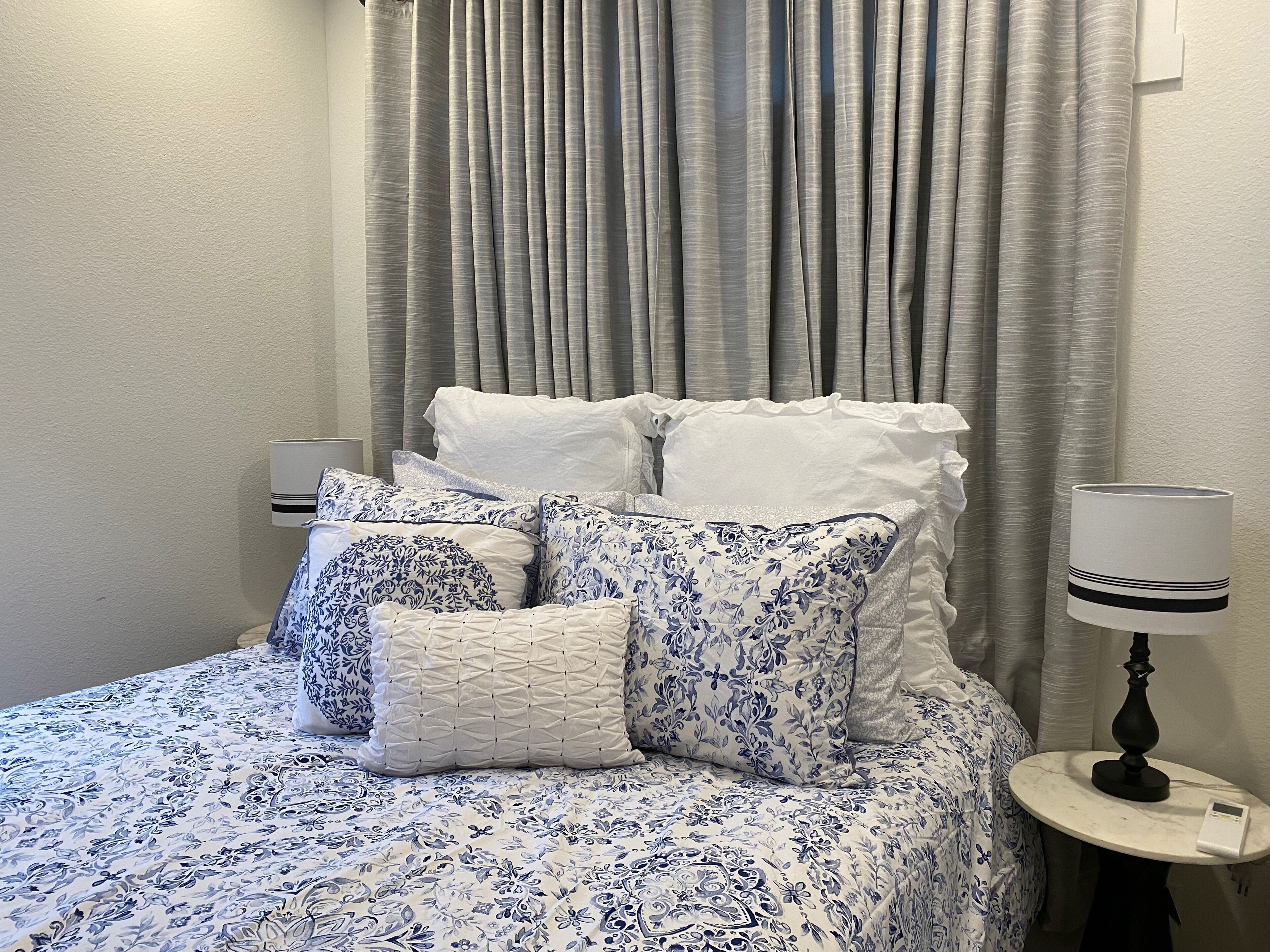 A neatly made bed with patterned bedding, a bedside table with a lamp, and a curtain backdrop.