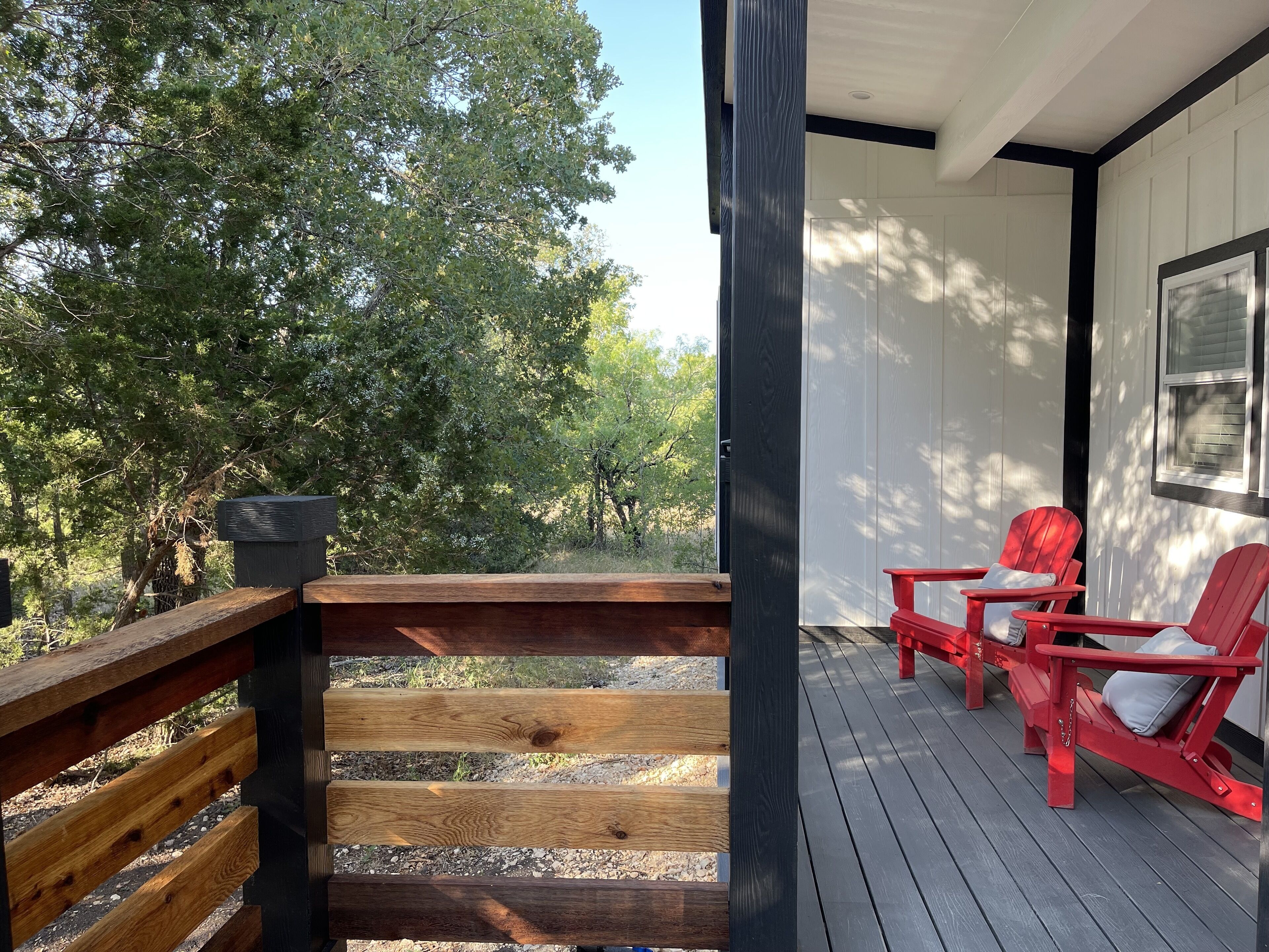A wooden deck with red Adirondack chairs and a view of trees.