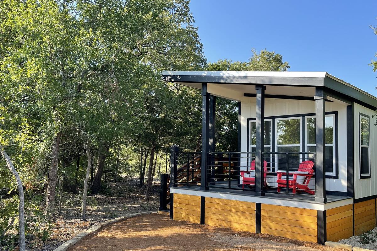 A modern cabin with a covered porch, a wooden deck, and a seating area with red chairs.