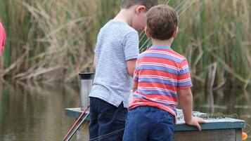 Two children fishing on a wooden dock with fishing rods and a metal container.