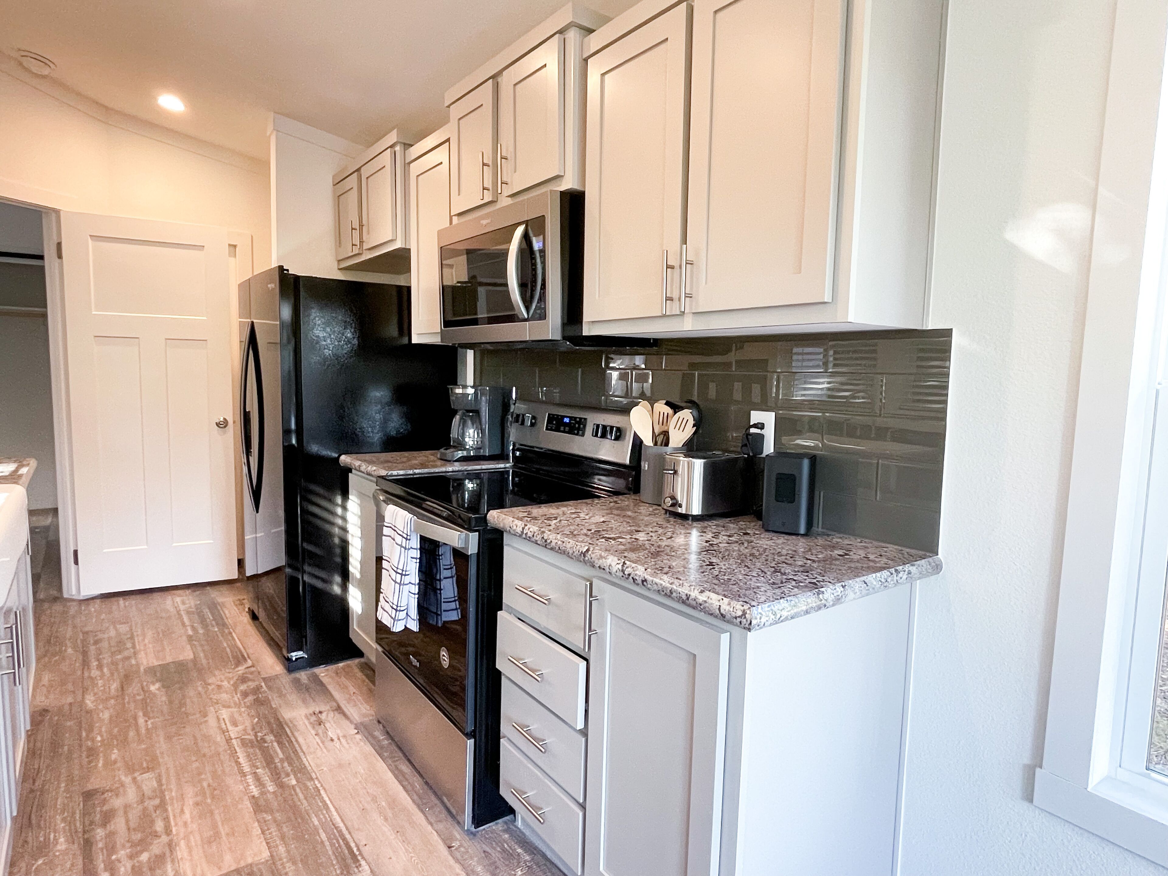 A modern kitchen with white cabinets, a black refrigerator, stainless steel appliances, and a granite countertop.