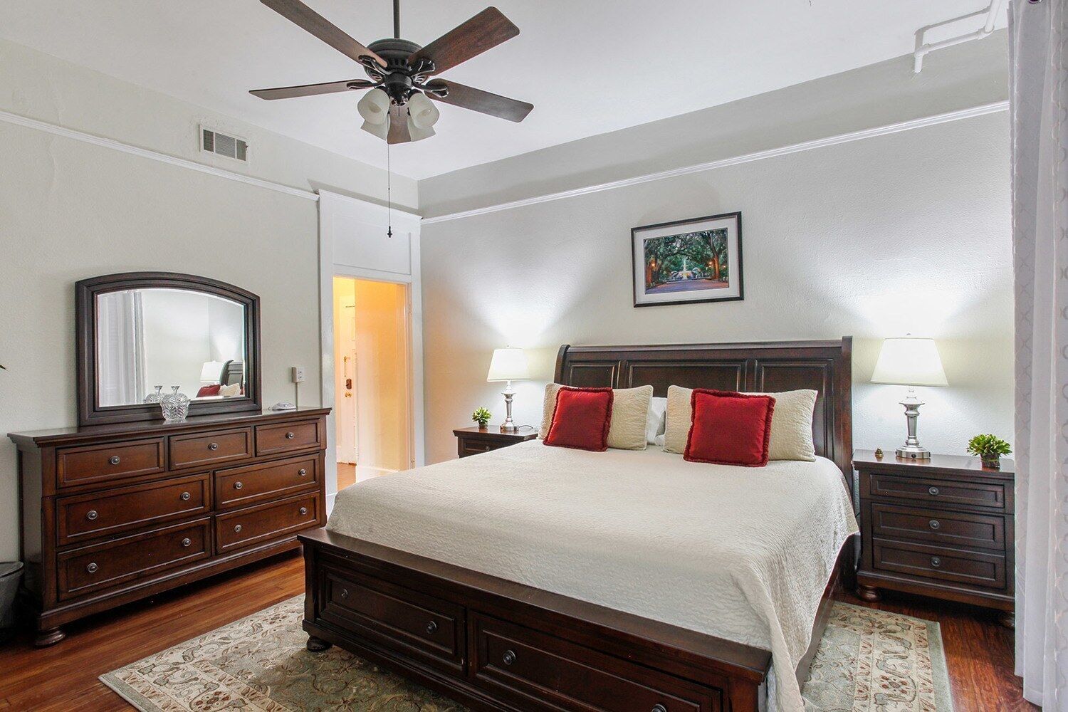 A bedroom with a large bed, wooden dresser, ceiling fan, and two bedside tables with lamps.