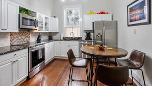 Una cocina moderna con armarios blancos, electrodomésticos de acero inoxidable, una mesa de comedor de madera y un cuadro con vistas a la ciudad.