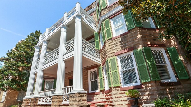 Un edificio histórico con balcón, fachada de piedra y contraventanas verdes.