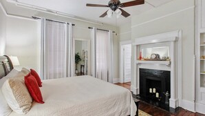 Un dormitorio con una cama grande, ventilador de techo, chimenea y vista al pasillo.