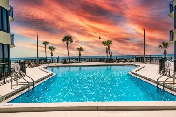 Una piscina con vista sul tramonto, circondata da palme e da una spiaggia.