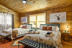 A wooden cabin room with two beds, a bench, a ceiling fan, and artwork on the walls. - Ultimate Mountain Escape Hot Tub Firepit  Lake Views Games (Morganton)