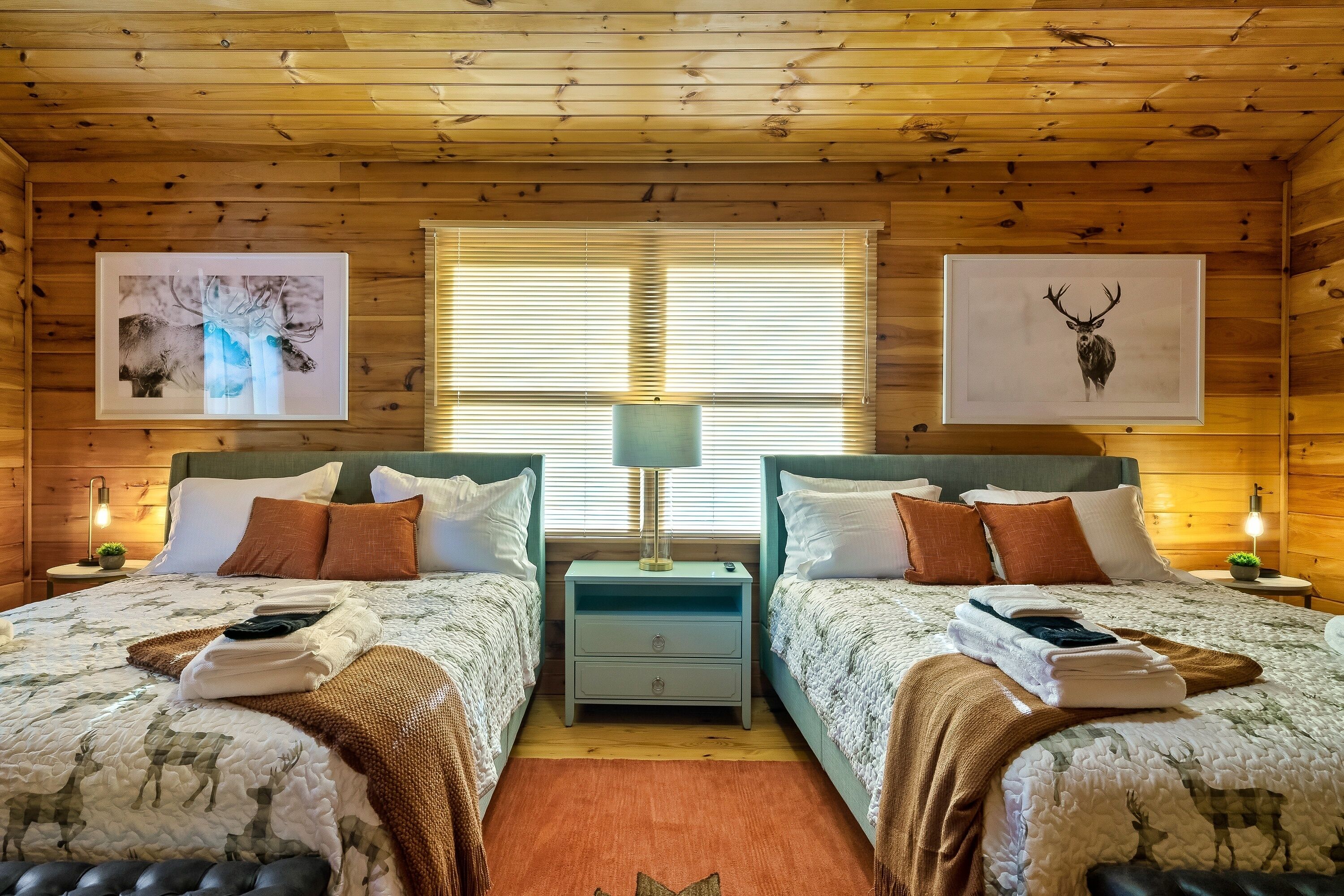 A cozy cabin room with two beds, wooden walls, and framed artwork.