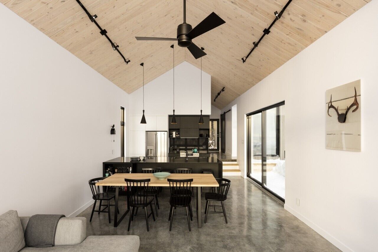A modern kitchen with a central island, black pendant lights, and a ceiling fan.