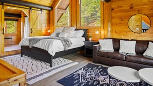 A wooden cabin interior with a bed, a sofa, a round table, and a mirror. - STUnning Views|Hot tub|FirePit|Easy Drive|Pool Table|Semi Secluded|Easy CheckOut (Sevierville)