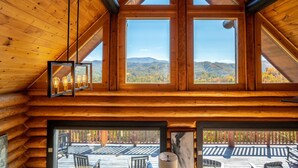 A log cabin interior with large windows offering mountain views, a wooden ceiling, and a deck visible through the windows. - STUnning Views|Hot tub|FirePit|Easy Drive|Pool Table|Semi Secluded|Easy CheckOut (Sevierville)