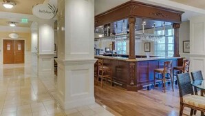 Um hall de hotel com área de bar, com banquetas de madeira e uma vitrine de vidro.