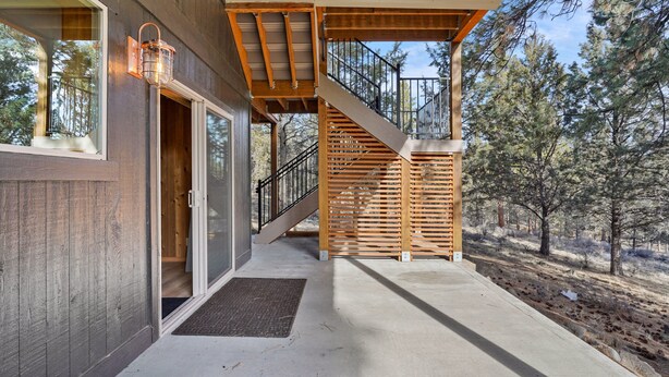 A wooden staircase leading to a covered outdoor area with a metal railing, surrounded by trees. - Pine Knoll - Peaceful, Hot Tub, Wifi, Propane Fire Pit, Newly Furnished (Bend)
