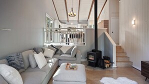 A modern living room with a sofa, ottoman, and a fireplace. - Pine Knoll - Peaceful, Hot Tub, Wifi, Propane Fire Pit, Newly Furnished (Bend)