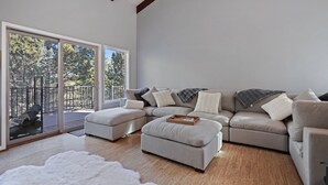 A modern living room with a sectional sofa, a white furry rug, and a wooden coffee table. - Pine Knoll - Peaceful, Hot Tub, Wifi, Propane Fire Pit, Newly Furnished (Bend)