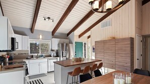 A modern kitchen with white cabinets, a wooden island, and a dining area with a wooden table and chairs. - Pine Knoll - Peaceful, Hot Tub, Wifi, Propane Fire Pit, Newly Furnished (Bend)