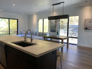 A modern kitchen with a large island, a dining area with a wooden table, and a sofa. - Ski in ski out Mountain Modern Townhouse (Whitefish)