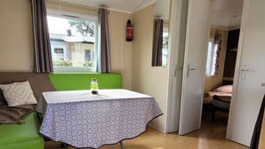 Une pièce avec un canapé vert, une table recouverte d’une nappe à motifs, un lit et un appareil de climatisation.