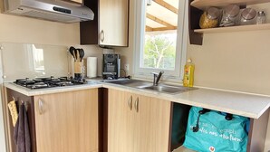 Une cuisine moderne avec des meubles en bois, une cuisinière à gaz, un four encastré, une fenêtre et une étagère avec des bocaux.