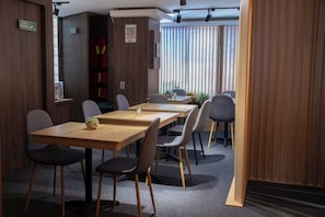 Una habitación de hotel moderna con una mesa de comedor de madera, seis sillas, una planta pequeña y una ventana con persianas.
