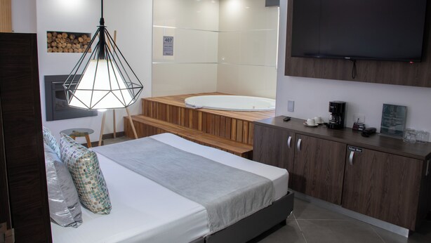 A modern hotel room with a bed, a wooden bench, a mini bar, a television, and a bathroom with a bathtub. - Hotel Velero (Rionegro)
