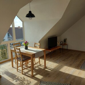 A cozy attic room with a dining table, chairs, a TV, and a potted plant. - Edder Apartment - a quiet and cozy vacation apartment with a large balcony (Edermünde)