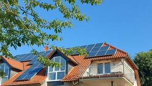 Ein zweistöckiges Gebäude mit rotem Ziegeldach, Solaranlagen und einem Balkon.