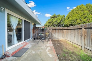 Un jardin à l’arrière d’une maison, avec une terrasse, une clôture en bois et un grand arbre.