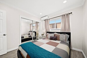 A bedroom with a bed, a bedside table, a mirror, and a window with curtains.