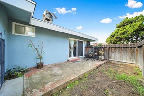 Un jardin à l’arrière d’une maison, avec une terrasse, une clôture en bois et un arbre.