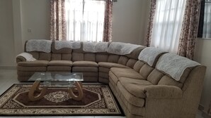 A sectional sofa with a glass coffee table and a patterned rug in a living room with sheer curtains. - Exquisite Accommodation in Gated Community (Versailles)