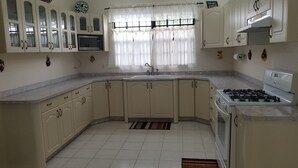 A kitchen with white cabinets, a microwave, a gas stove, and a window with curtains. - Exquisite Accommodation in Gated Community (Versailles)