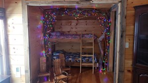 Een gezellig chaletinterieur met een houten stapelbed, een schommelstoel en een klein bureau.
