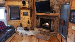 Een gezellig cabin interieur met een stenen openhaard, houten wanden, een leren bank en een bevestigde televisie.