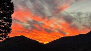 Een rustig meer dat een levendige zonsondergang weerspiegelt, met heuvels op de achtergrond.