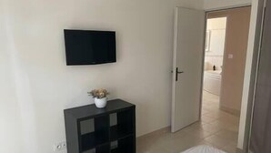 A bedroom with a bed, a TV mounted on the wall, and a door leading to a bathroom. - To complete (Aramon)