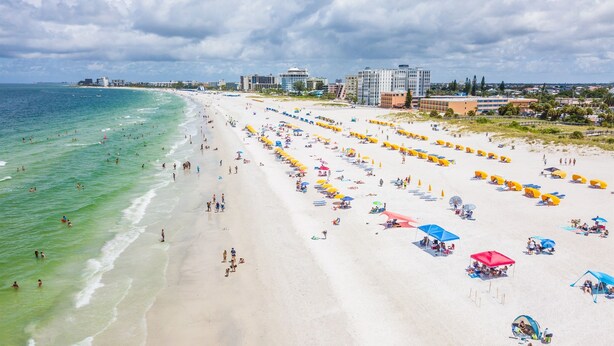 A beach with rows of umbrellas and beach chairs, a sandy shore, and buildings in the background. - Beach Haven in South Clearwater Beach (Clearwater Beach)