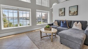 A spacious living room with a grey sofa, a round coffee table, and a view of the sea through large windows. - Beach Haven in South Clearwater Beach (Clearwater Beach)