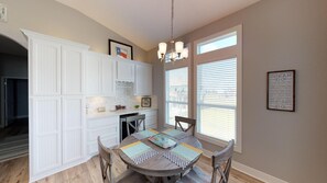 A kitchen with white cabinetry, a dining table with placemats, and a chandelier. - Kool Breeze Escape: 3 BR, 2 BA House in Port Bolivar, Sleeps 12 (Bolivar Peninsula)