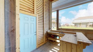 Una cabana de fusta amb una porta de blau clar, una cadira de fusta i una finestra que fa vedar a una zona residencial.