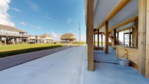 Un edifici a la costa amb un porxo cobert, un camí de formigó i una zona enjardinada.
